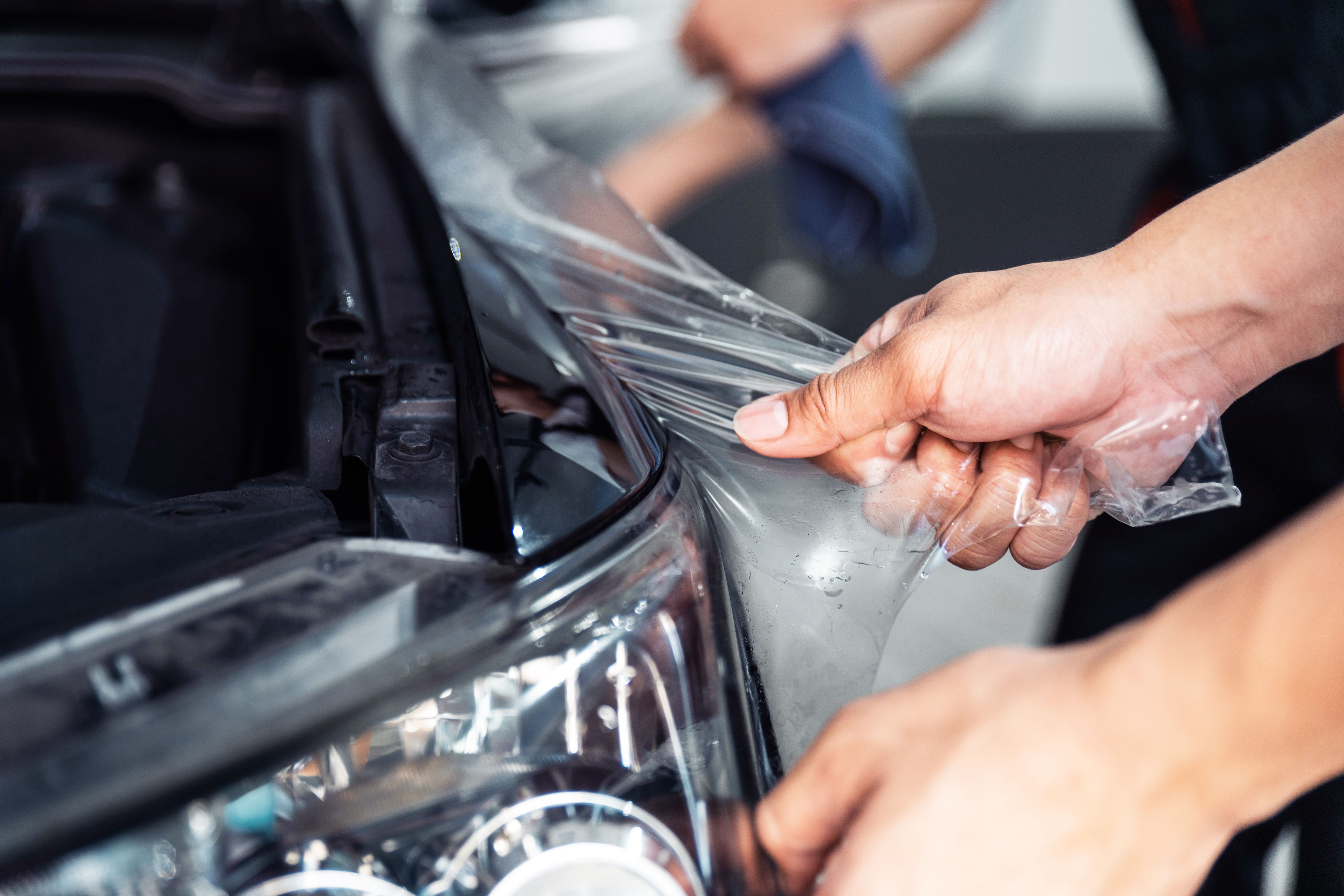 PPF installation process, close-up stretching removing an old transparent film on a car headlight and hood by hand. Automobile professional service.